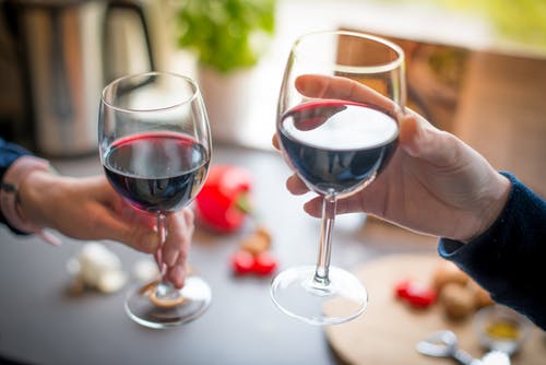 Two people clinking red wine glasses
